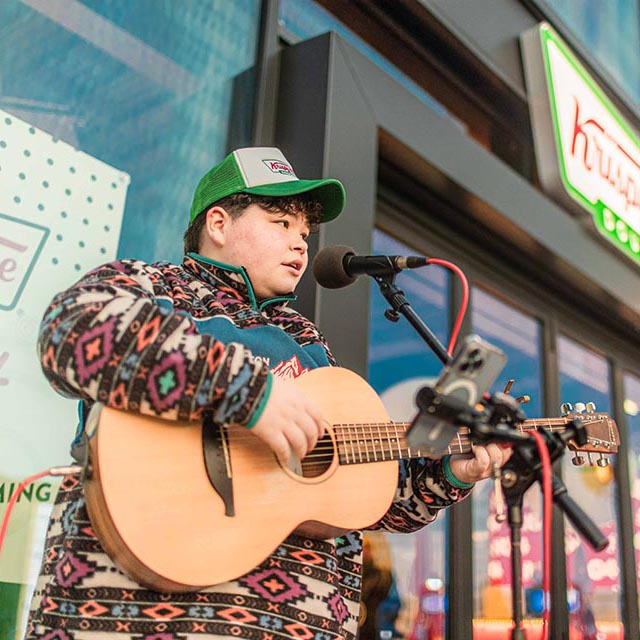 Young man in a cap plays guitar outside a Krispy Kreme shop