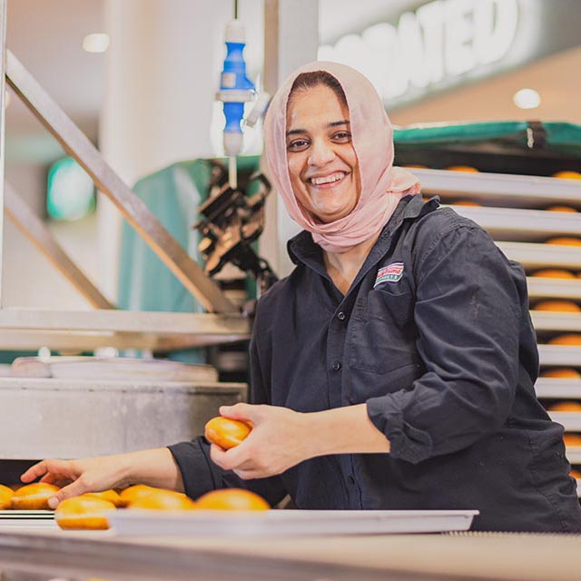 Woman in coveralls and headscarf collects donuts in the factory