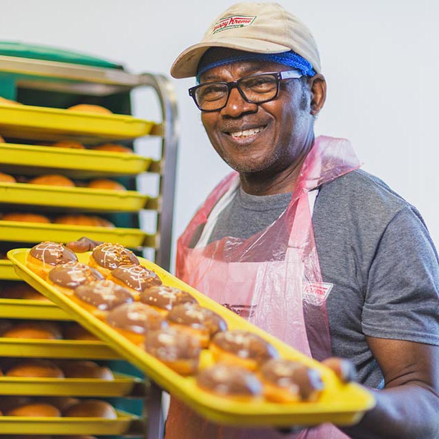 Smiling man holds a tray of fresh donuts in a factory