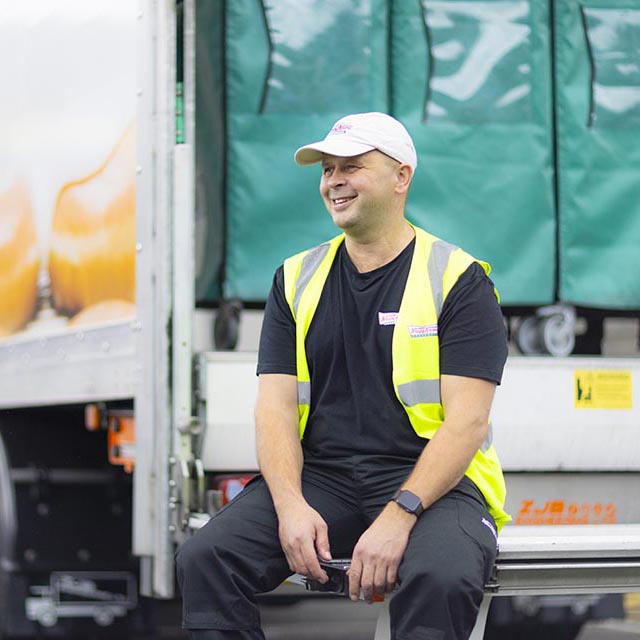 Man in a cap and hi-viz sits on a lorry tailgate
