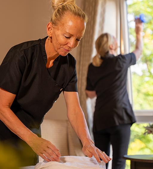 woman making the bed while another cleans the window