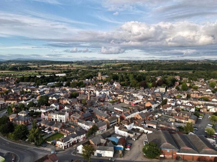 Aerial view of a market town surrounded by green countryside, with a church tower at its centre and rolling hills in the distance.