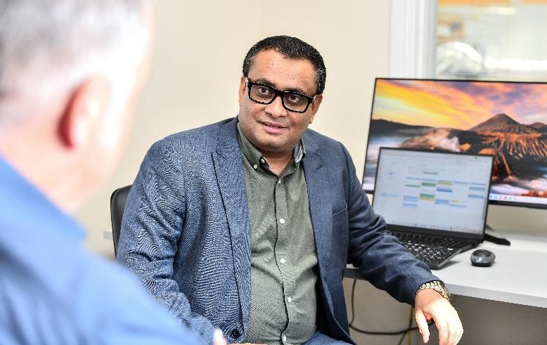 A middle aged man seated at a desk listens to an explanation