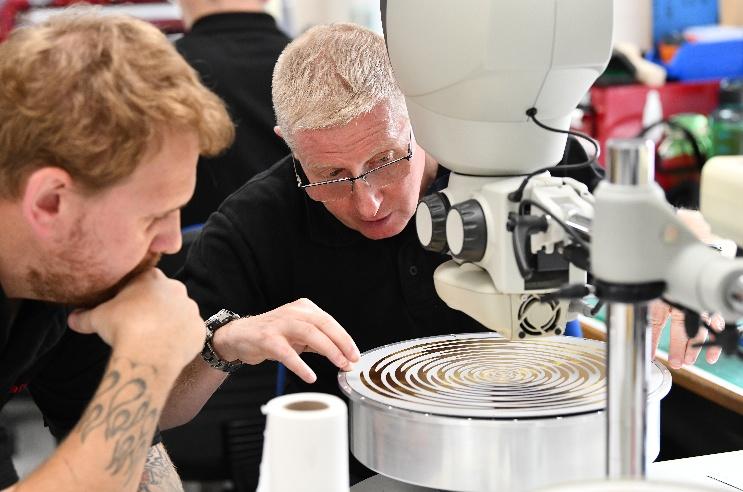 A young bearded man receives advice from an older technician