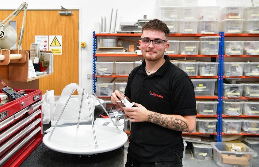 I young technician smiles towards the camera while assembling a dish array