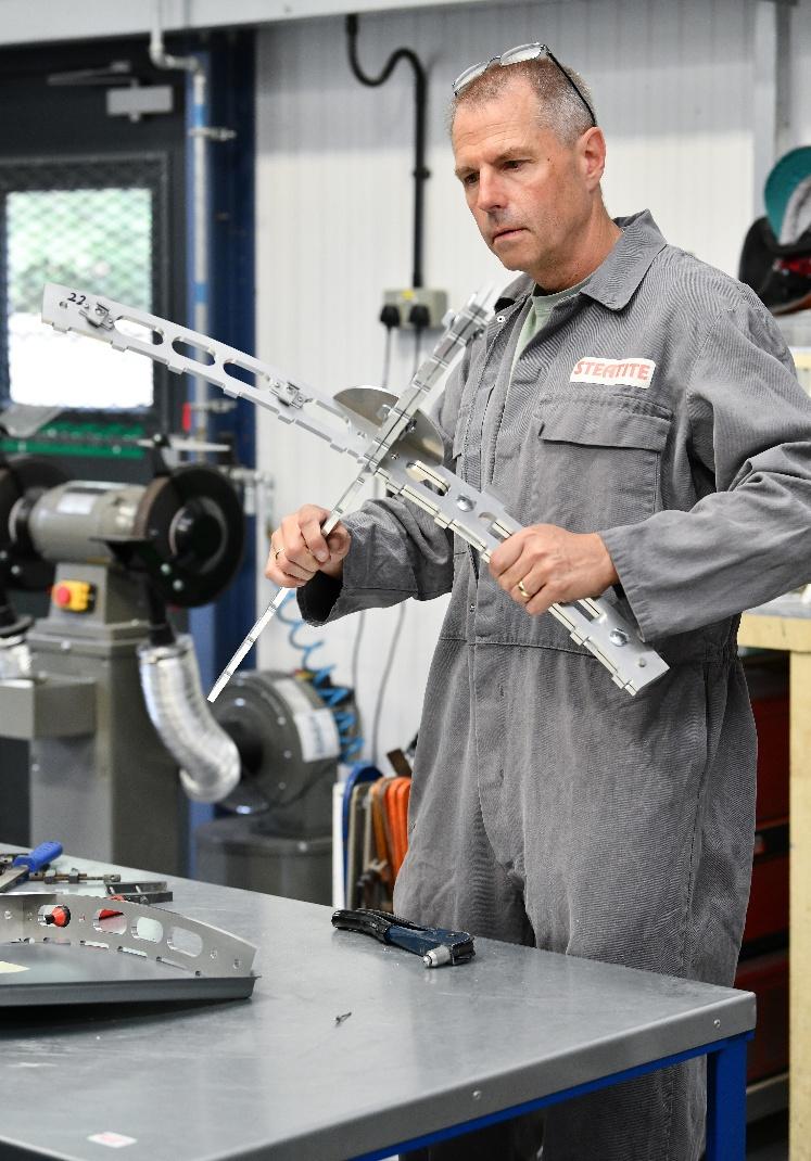 married man in grey overalls works on the support struts of a dish antenna