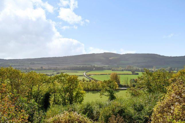 A view over green fields and hedgerows toward rolling hills under a partly cloudy sky.
