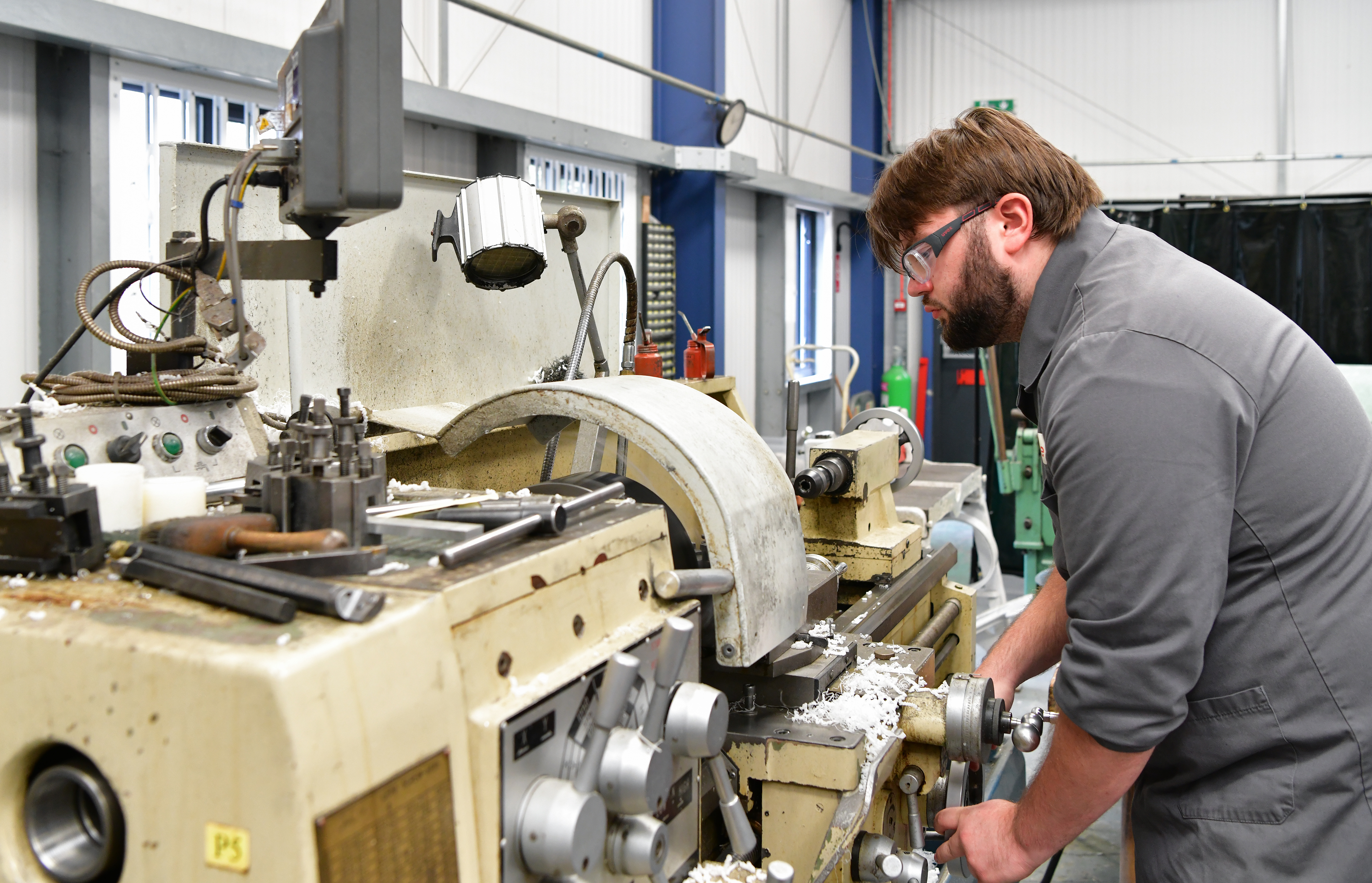 Bearded man in safety glasses operates a lathe