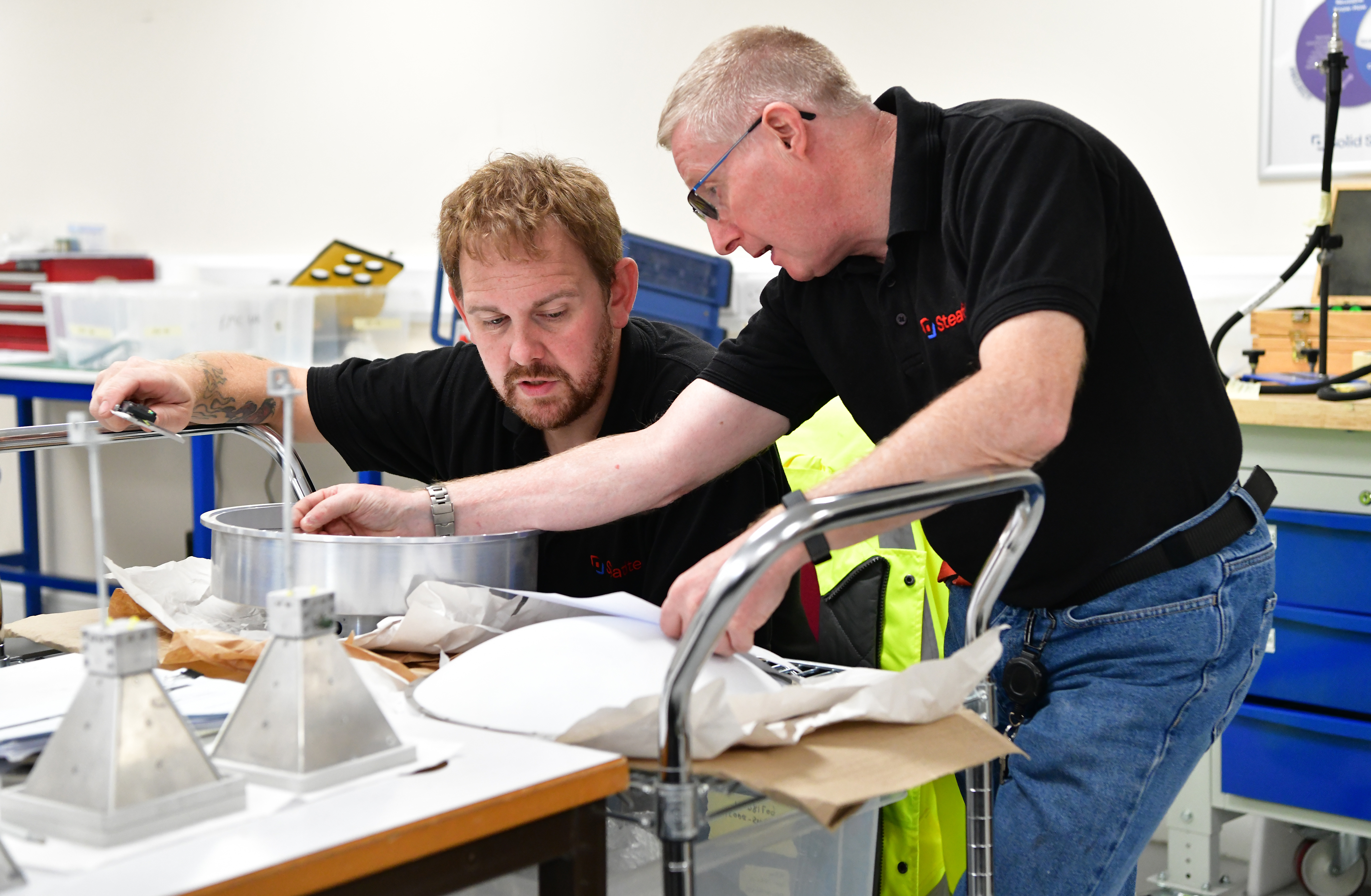 A young man with a beard receives traing from an older technician