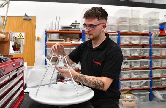 A trainee technician wearing safety glasses assembles a dish antenna