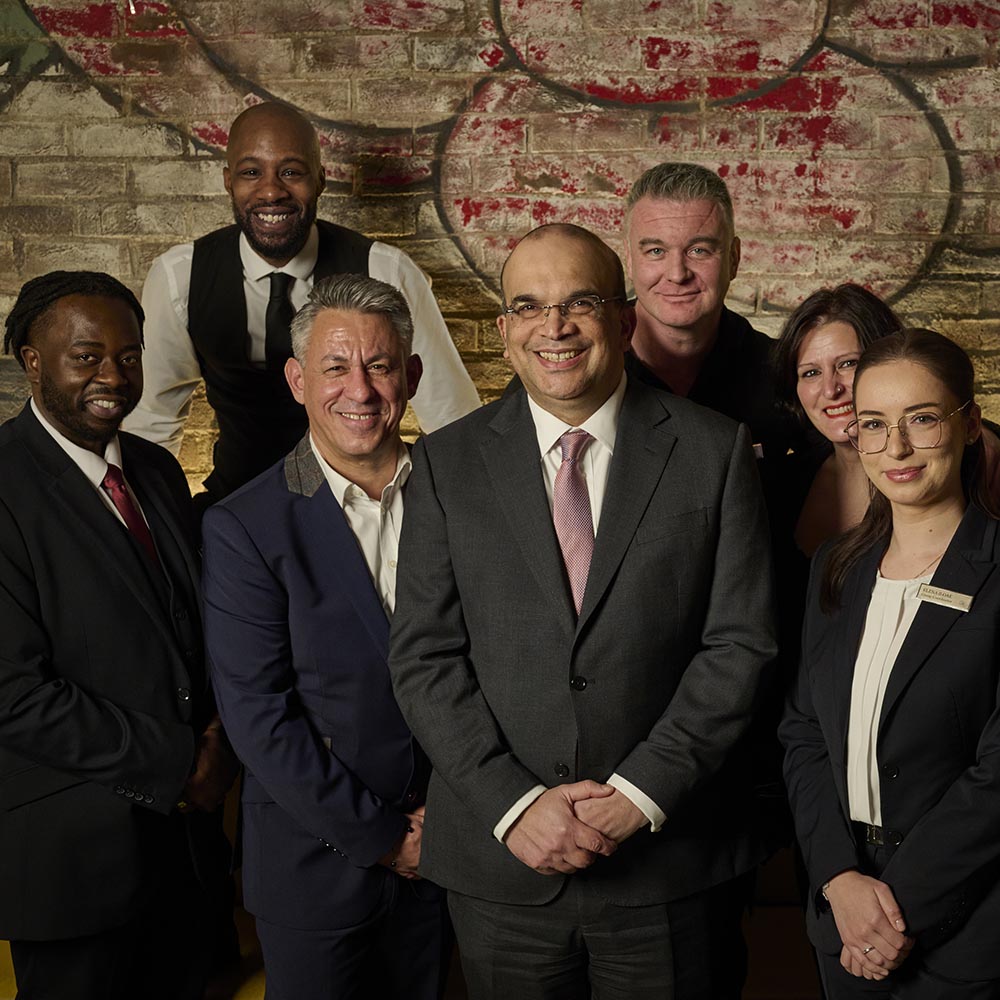 a diverse group of men and women smile infront of a mural